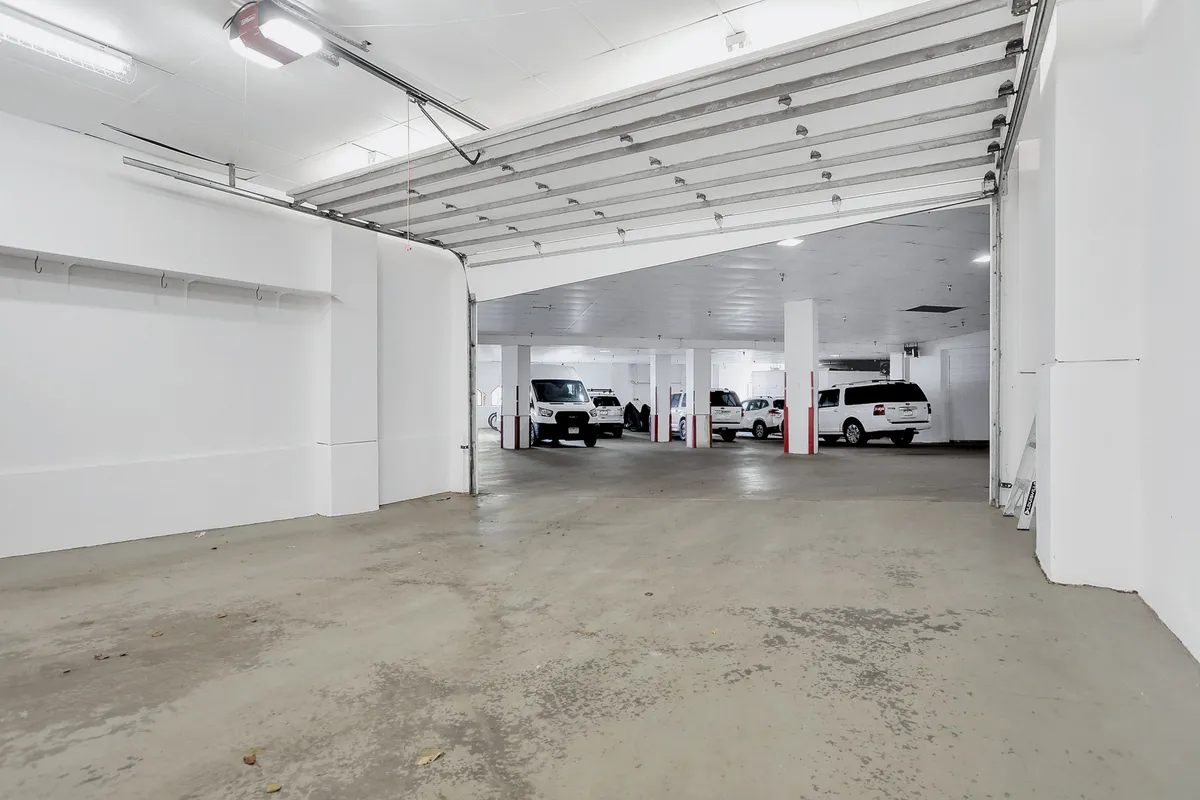This image shows a garage entrance with parked vehicles and white walls. The space is clean, well-lit, and organized, emphasizing ease of access and security for vehicles and gear storage.