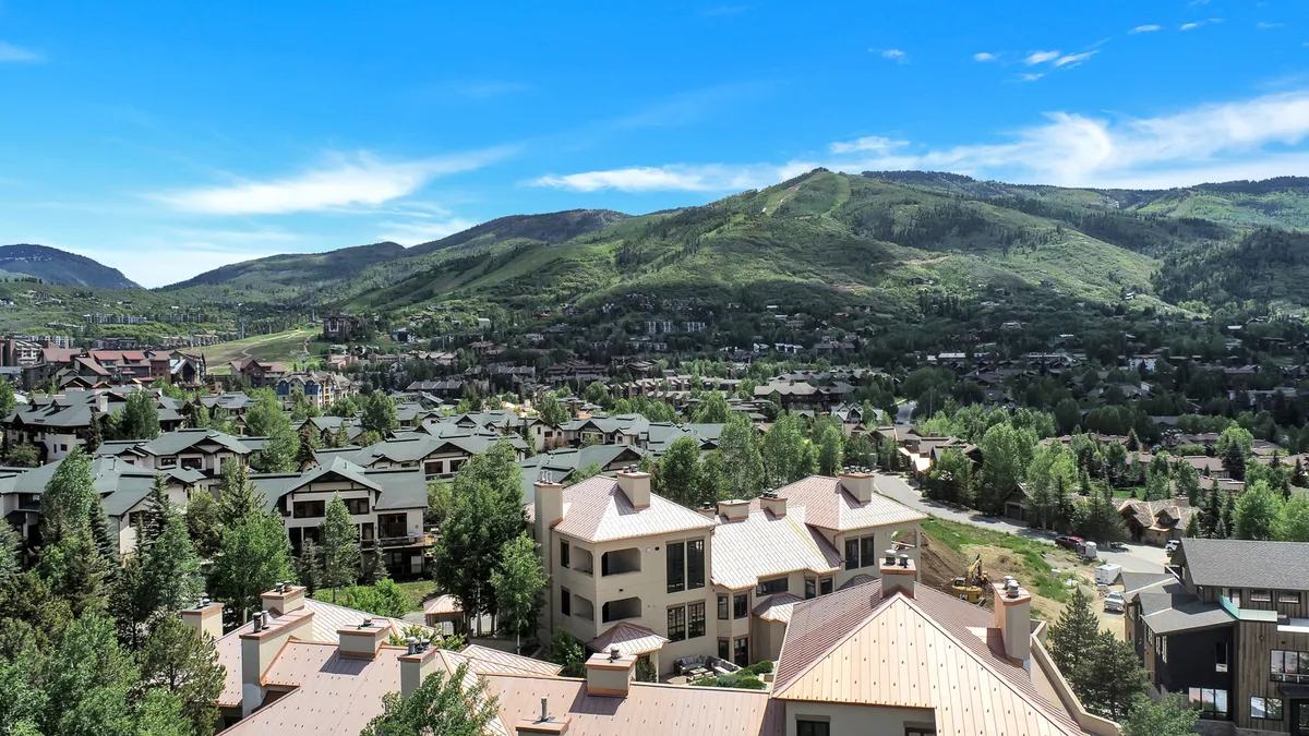 A sweeping view of the surrounding mountains and residential area, with a tree line in the foreground. The image emphasizes the breathtaking natural landscape and the community's immediate access to hiking and biking opportunities.