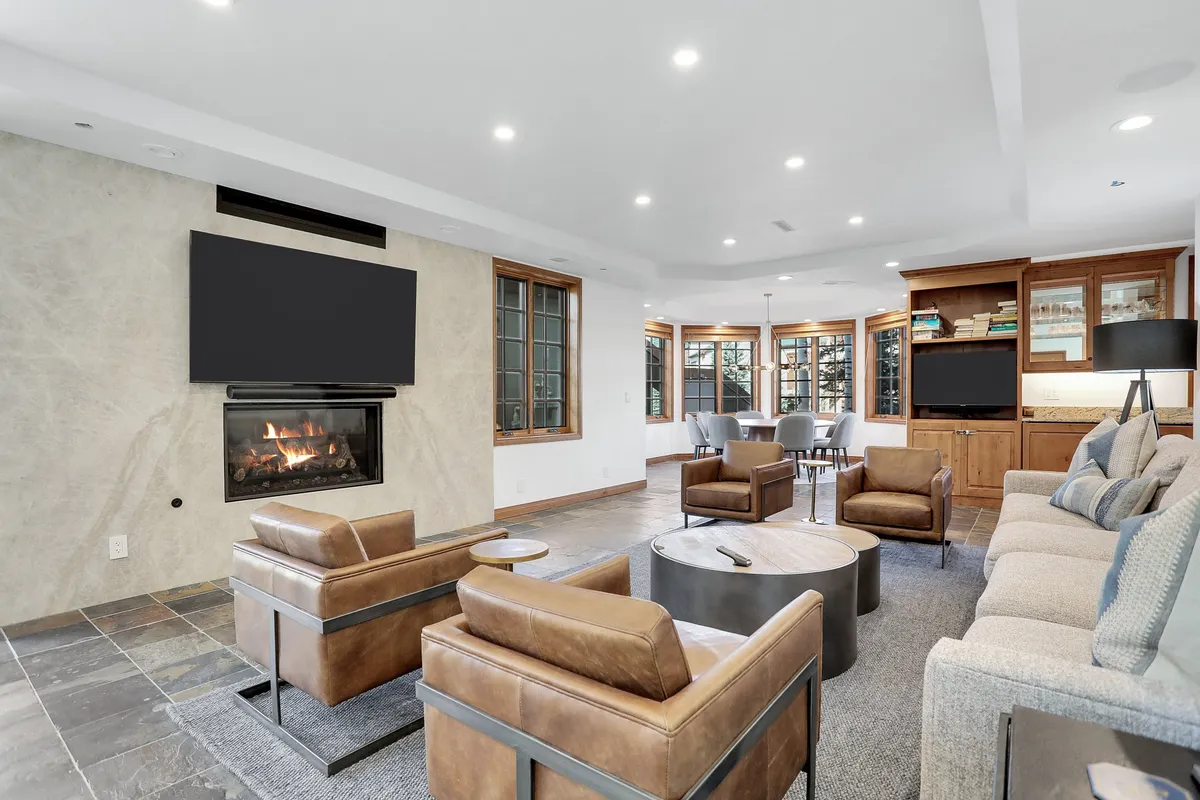 This image showcases a cozy living room featuring a modern fireplace, plush seating, and large windows that bring in natural light. The arrangement is ideal for gathering, with comfortable sofas oriented towards the fireplace and a large TV, evoking an inviting atmosphere for movie nights or game sessions.