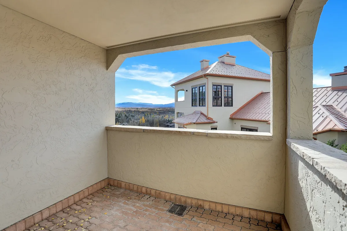 This image captures a serene balcony with open views of the surrounding mountains and neighboring architectural details. The balcony space is inviting with a tranquil mood, ideal for enjoying a morning coffee or unwinding in the evening while taking in the expansive scenery.