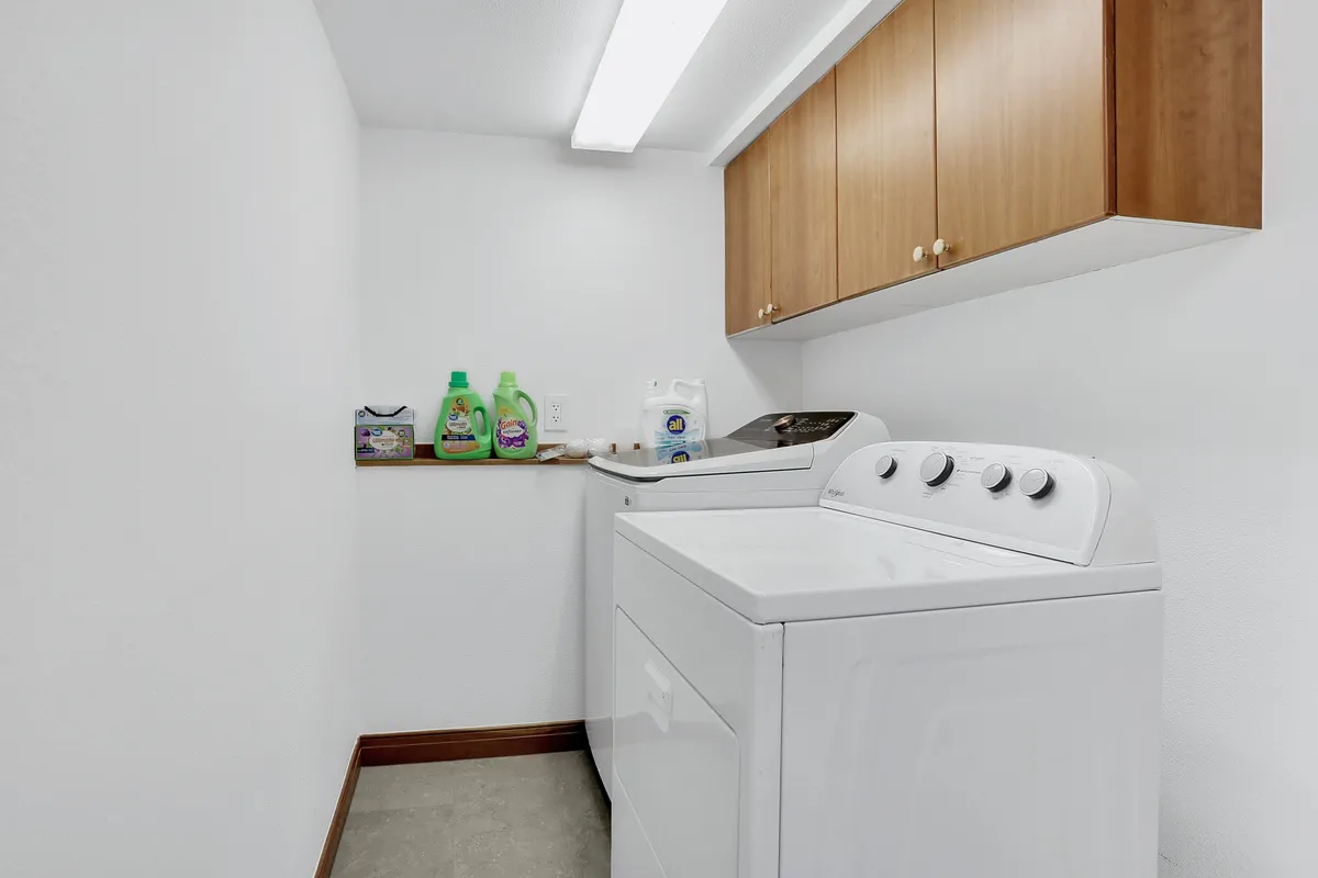 A laundry area featuring a washing machine, dryer, detergent bottles, and a shelf with cleaning supplies. The space is tidy and organized, emphasizing functionality and the ease of handling post-adventure messes.