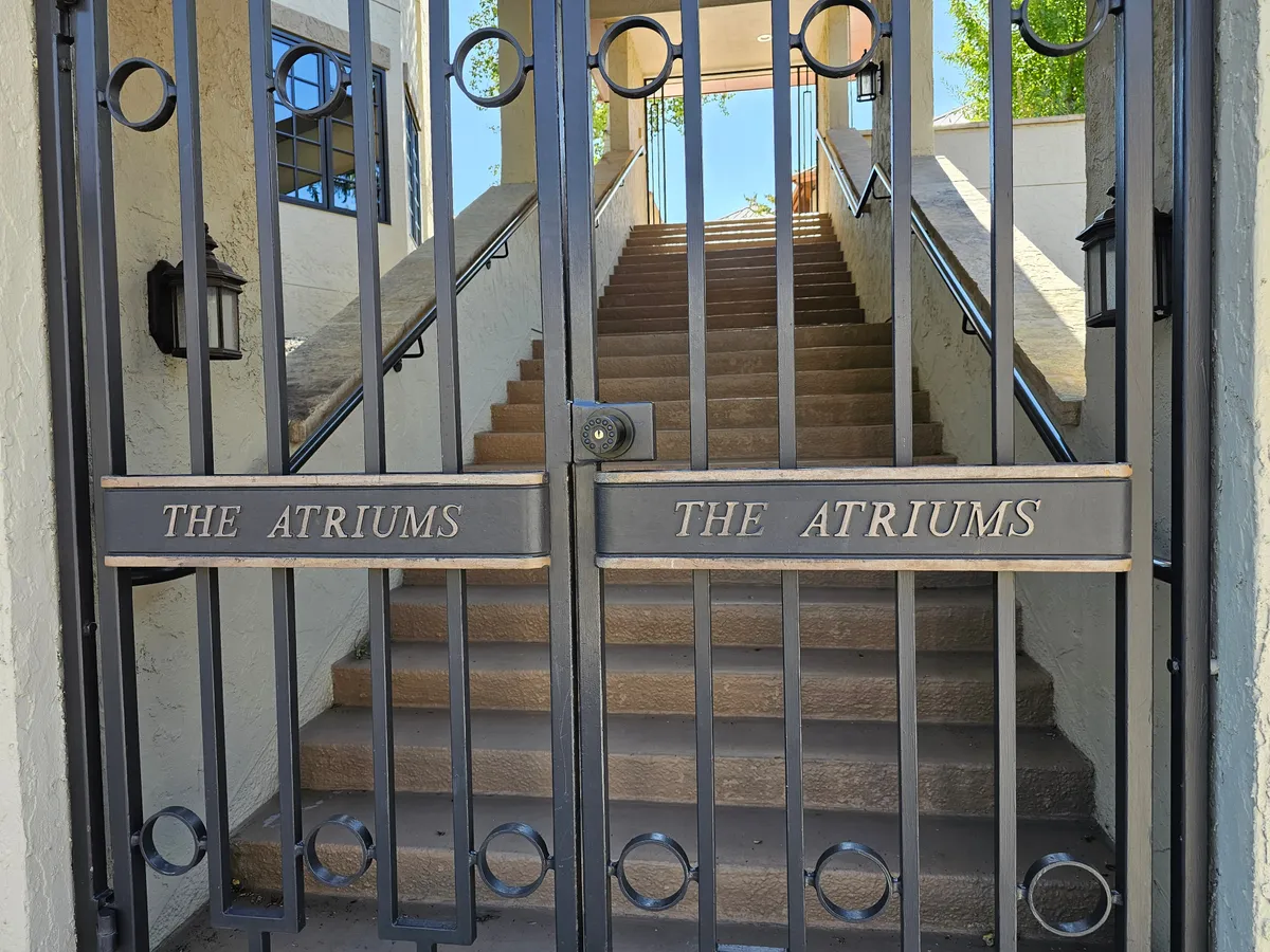 This exterior image shows the gated entrance and staircase leading into The Atriums, conveying a sense of security, exclusivity, and arrival. The inviting mood and clear signage emphasize the community's prestige and the rare sense of privacy inside.