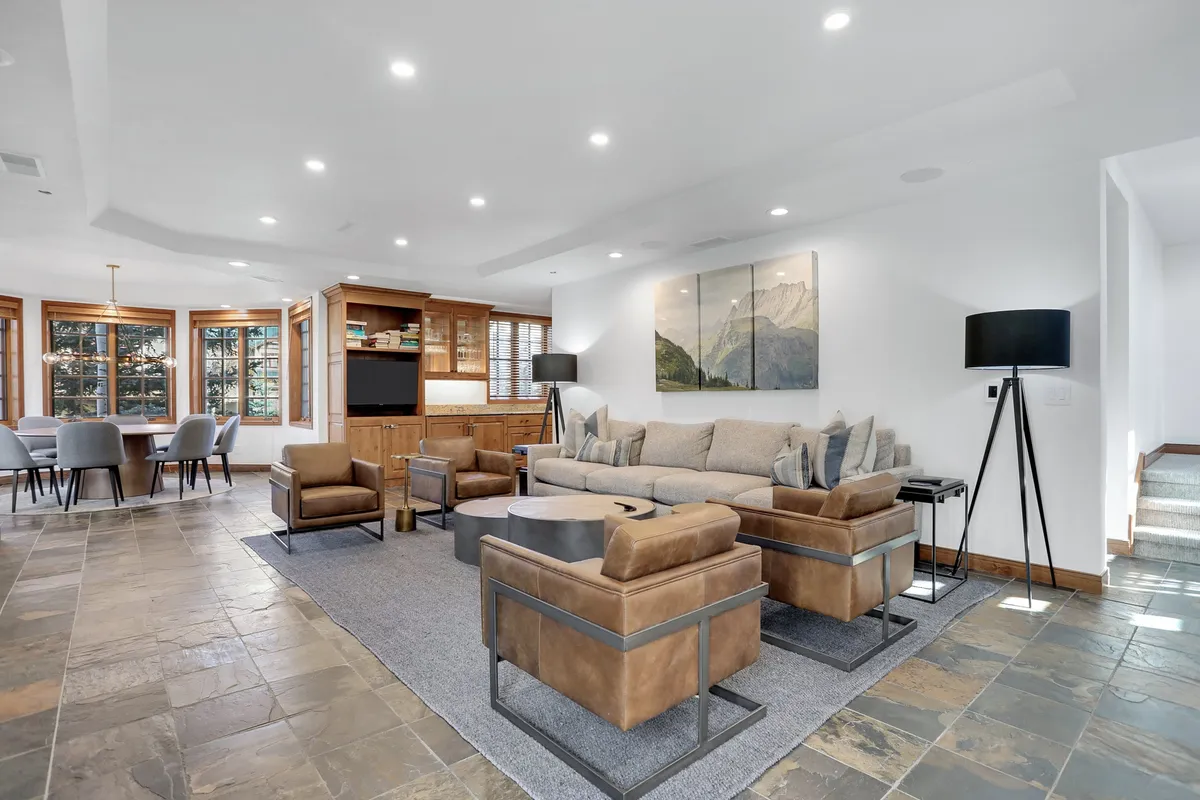 This scene captures an open-concept living and dining space, with a comfortable sofa, artwork, a coffee table, wooden cabinetry, and a dining table visible in the background. The layout emphasizes flow and multifunctional use, suitable for both relaxing and entertaining guests.