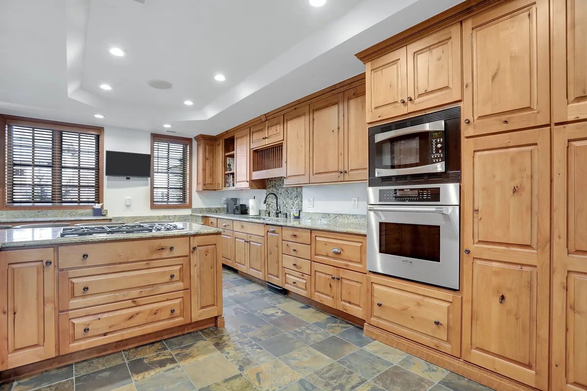 A modern kitchen with wooden cabinetry, granite countertops, a generous kitchen island, and high-end appliances. The setup is spacious and practical for preparing group meals and features seating at the breakfast bar, emphasizing culinary experiences and social interaction.