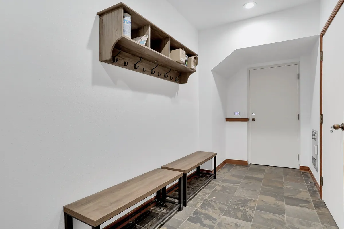 A mudroom-style entry with wooden benches, a shelf with hooks, and clean white walls. The scene feels organized and welcoming, providing a spot to hang coats and sit while changing footwear.