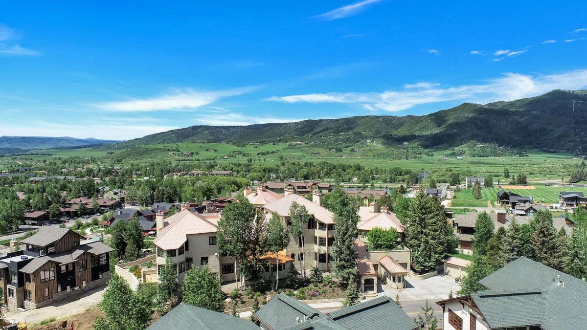 This exterior image features the Atriums residential buildings surrounded by lush greenery and distant mountain views. The scene captures the serene atmosphere of the neighborhood and hints at the proximity to outdoor adventure with both natural and architectural elements in the frame.