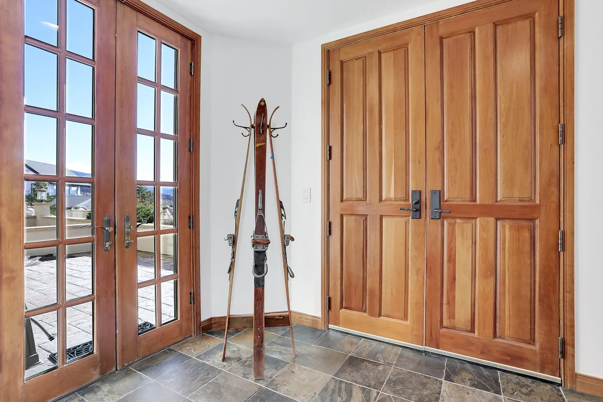An inviting entryway featuring wooden double doors, large windows, and a ski rack with skis, welcoming residents home after a day outdoors. The design blends functionality (gear storage) with a cozy, welcoming atmosphere.