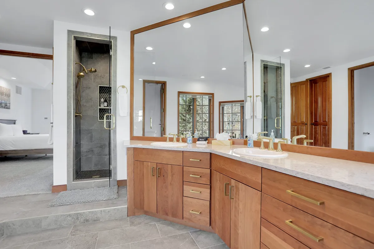 A spacious bathroom featuring a double sink vanity, a large walk-in shower, expansive mirrors, and natural light flowing in through the windows. The space feels open, fresh, and perfect for restful routines.