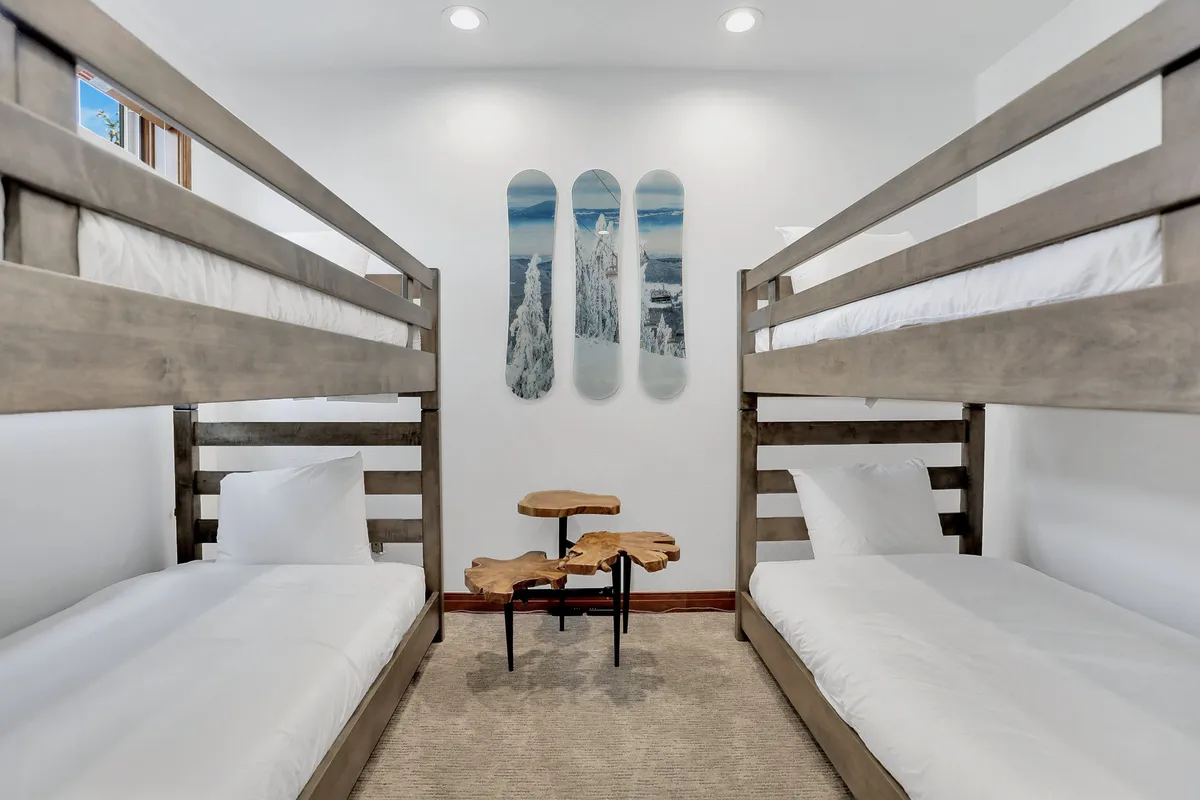 A bright and playful bunk room with stacked bunk beds, cheerful artwork, and a wooden side table. The space feels friendly and fun—clearly designed with kids and sleepovers in mind, hinting at storytelling and games.